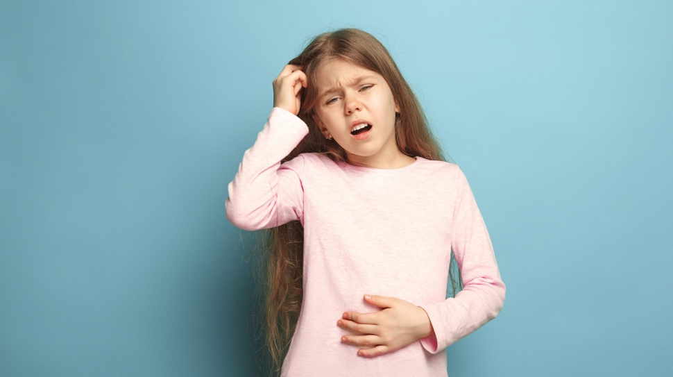 The abdominal pain. The sad teen girl with abdominal pain on a blue studio background. Facial expressions and people emotions concept. Trendy colors. Front view. Half-length portrait