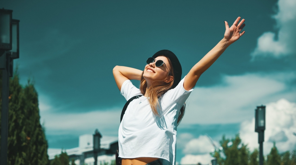 Freedom young woman carefree and happy with open arms on blue sky with hypnotizing sky in background. Caucasian girl in white shirt and jeans, feeling happiness enjoying her travel vacation