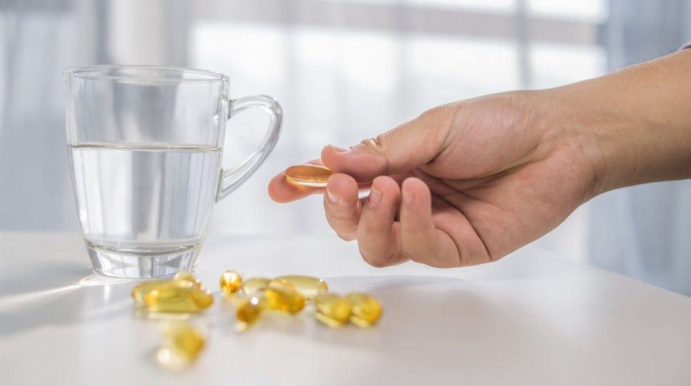 healthy lifestyle, medicine, nutritional supplements and people concept - close up of male hands holding pills with cod liver oil capsules and water glass