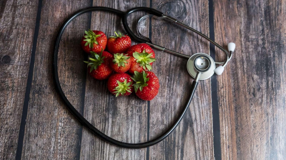 Stethoscope with strawberries and black seedless grape on top of wooden table. Medical and healthcare conceptual.