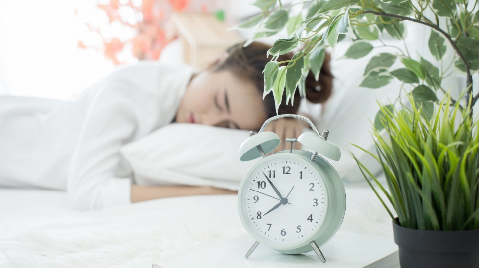 woman asleep in bed while her alarm shows the early time at home in bedroom