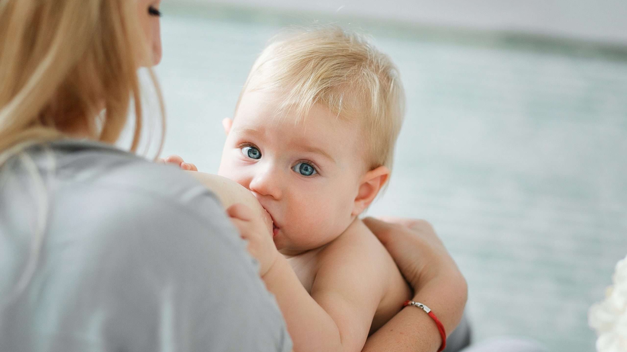Woman breasrfeeding little baby. Mother with her newborn daughter. Rear view through shoulder.