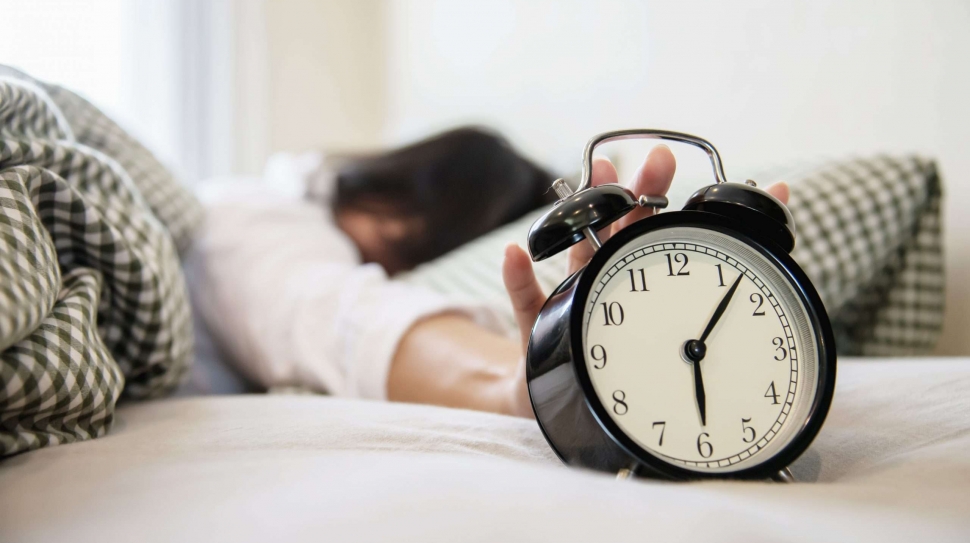Sleepy woman reaching  holding the alarm clock in the morning with late wake up - every day life at home concept