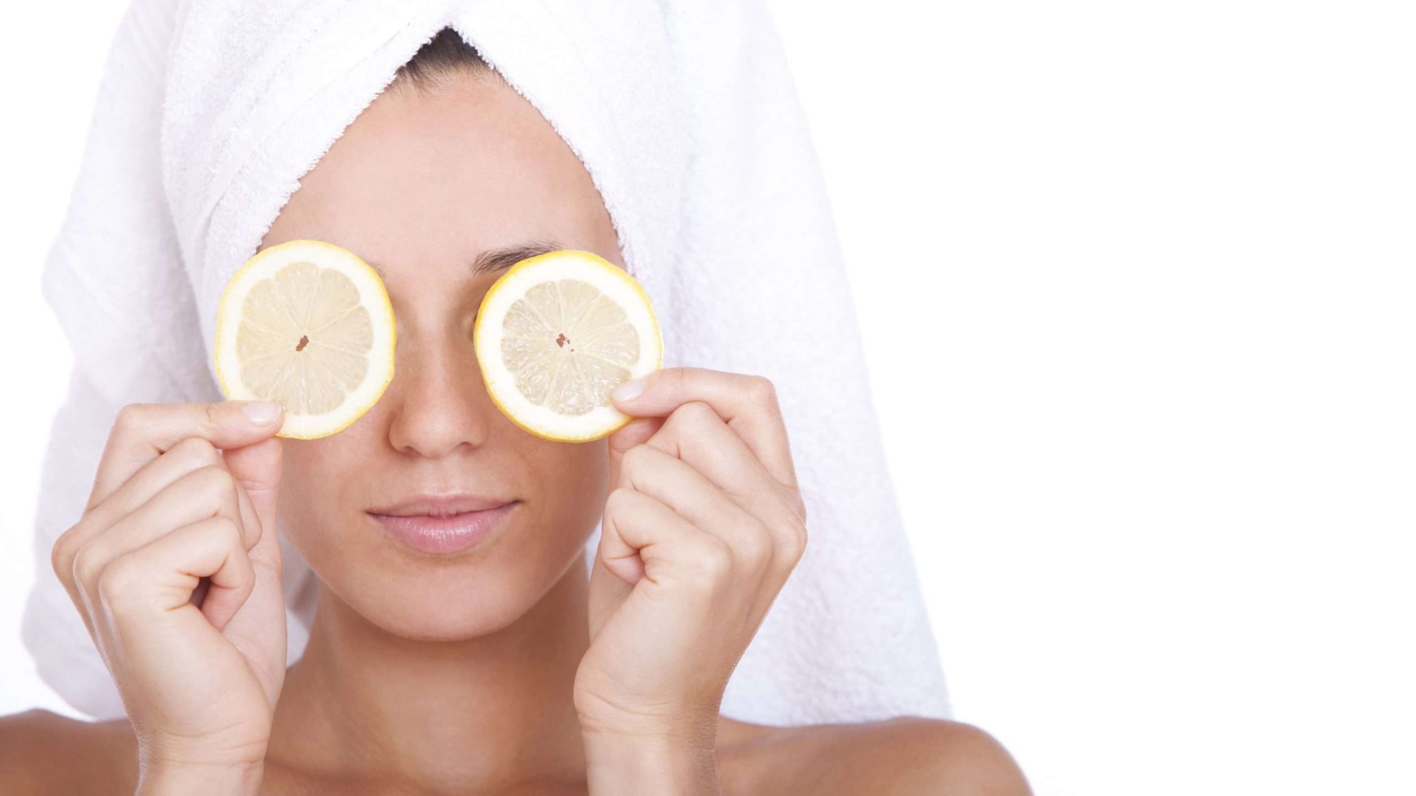 Woman with clean face is holding two slices of lemon over white background
