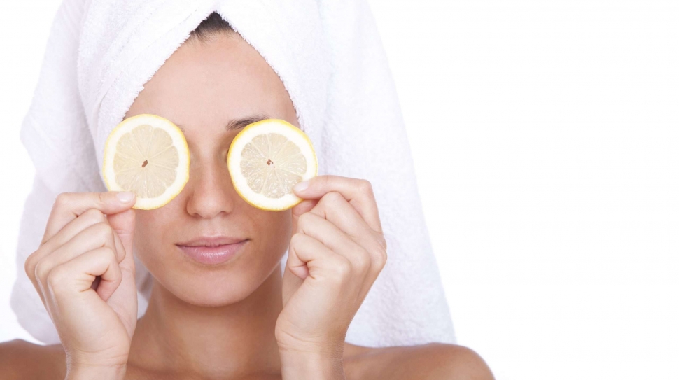 Woman with clean face is holding two slices of lemon over white background