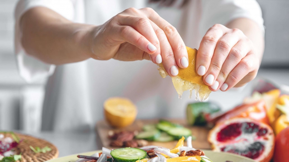 A woman makes a salad of fresh vegetables, squeezes the juice of a lemon, close-up, the concept of diet and healthy eating.