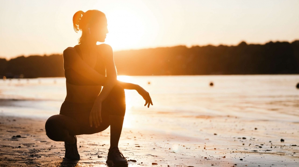 Young sportswoman crouching by the river and enjoying in the morning sun. Copy space.