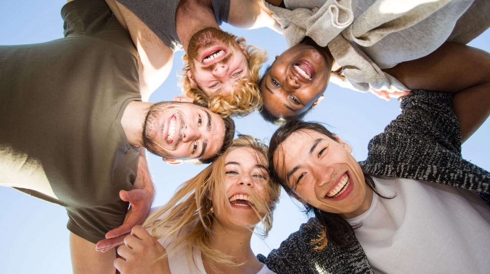 Cheerful friends huddling against blue sky on sunny day
