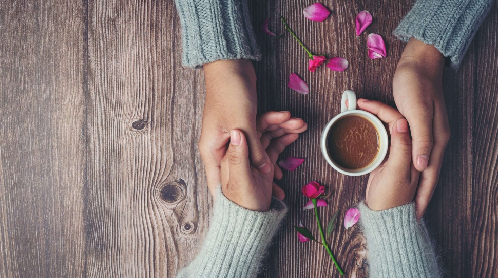 Two people holding cup of coffee in hands with love and warmth on wooden table